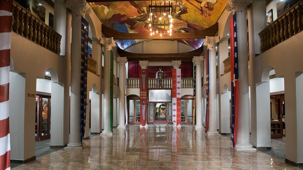 Un vaste hall d’entrée avec un sol en marbre, de grandes colonnes et un plafond haut orné d’un lustre.