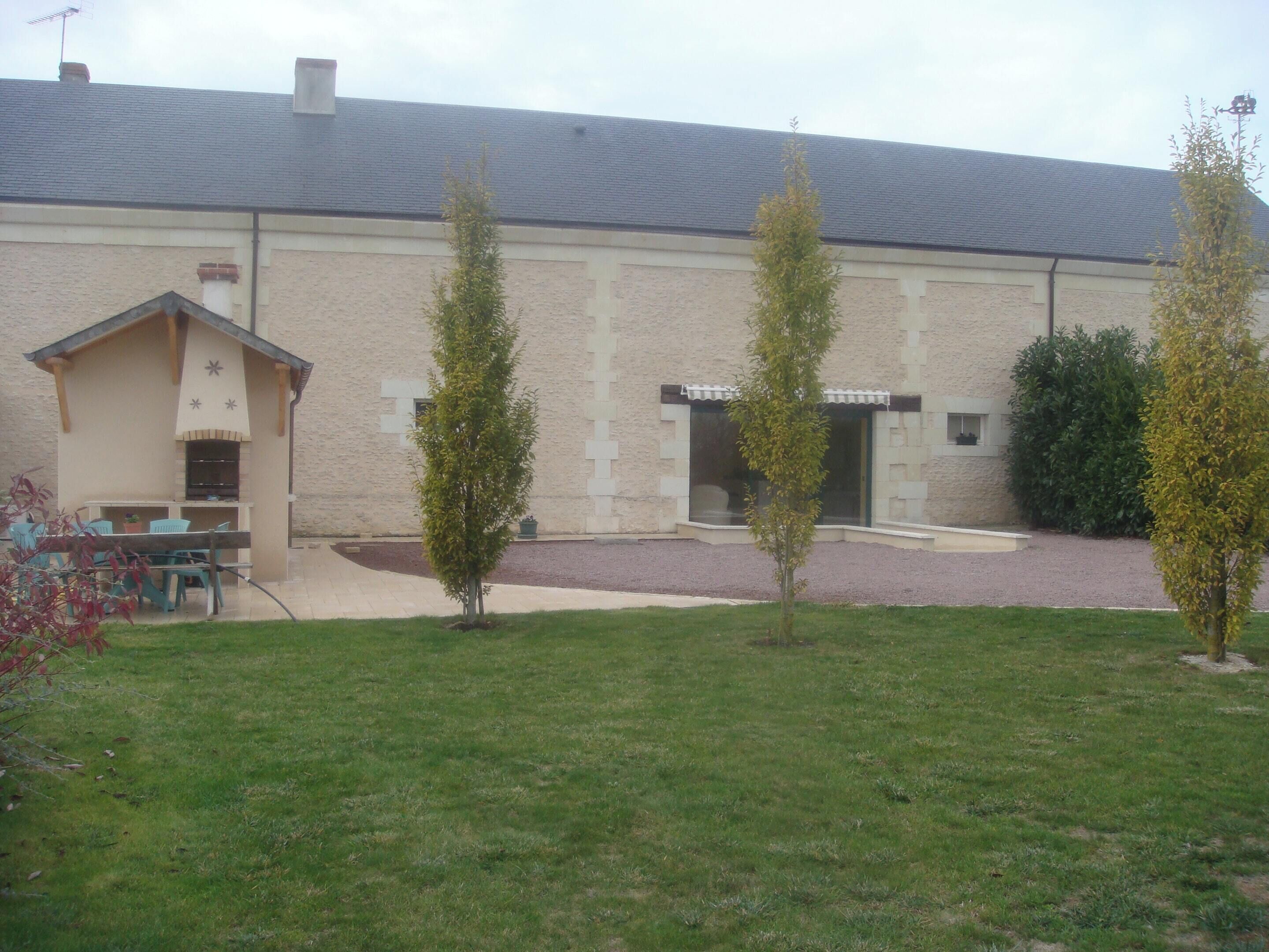 A building with a tiled roof, a small outdoor seating area with chairs and a table, and a paved driveway.