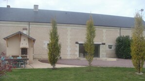 Un edificio con tejado de tejas, un pequeño espacio al aire libre con sillas y una mesa, y un camino de entrada pavimentado.