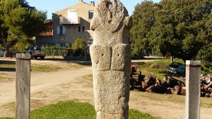 Un monument de pierre situé dans un espace verdoyant, avec un bâtiment et des arbres en arrière-plan.