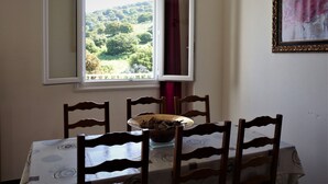 Un coin repas avec une table dressée pour quatre personnes, une fenêtre donnant sur un paysage verdoyant et une œuvre d’art encadrée accrochée au mur.