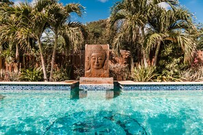 A pool with a Buddha statue in the center, surrounded by palm trees and a wooden fence. - A private vacation villa with gorgeous pool. (Kralendijk)