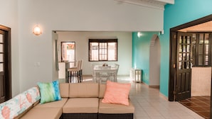 A living room with a sofa, a dining table, and chairs. There is a kitchen area in the background. - A private vacation villa with gorgeous pool. (Kralendijk)