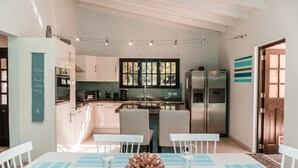A modern kitchen with white cabinets, a central island, and a dining area with white chairs and a table. - A private vacation villa with gorgeous pool. (Kralendijk)