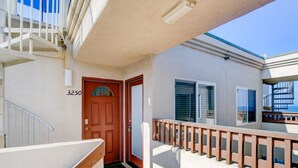 A residential building with a red door, white exterior walls, and a balcony with a wooden railing.