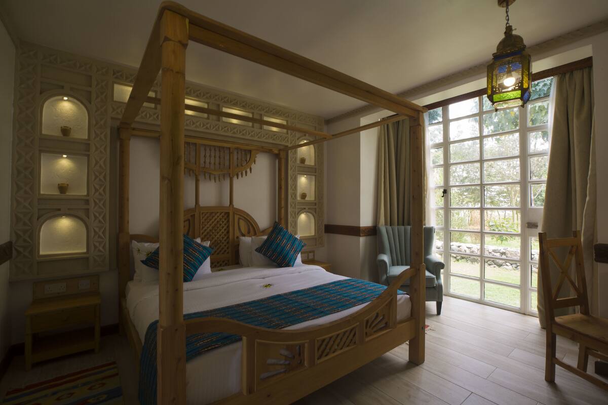 Uma cama de dossel com estrutura de madeira e cortina, uma janela grande com cortinas e um candeeiro pendente.