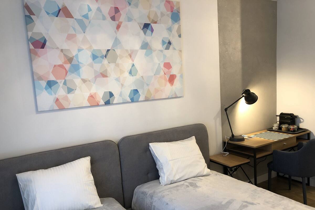 Quarto com duas camas, uma escrivaninha com abajur e uma máquina de café.