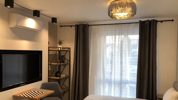 A modern hotel room with a large bed, a desk with a chair, a TV, a bookshelf, and a chandelier. - Like at Home Warsaw (Warsaw)