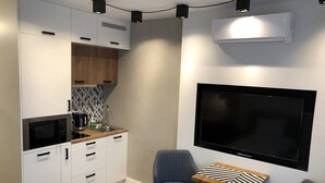 A compact kitchen with white cabinets, a microwave, and a sink. There is a small table with chairs and a flat-screen TV mounted on the wall. - Like at Home Warsaw (Warsaw)