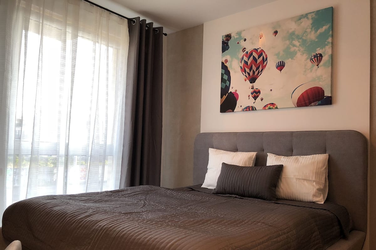 Quarto com uma cama grande, cabeceira cinzenta e um quadro de balões de ar quente na parede.