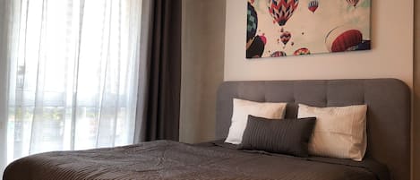 A bedroom with a large bed, a grey headboard, and a painting of hot air balloons on the wall.