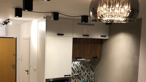 A compact kitchen with white cabinets, a microwave, and a sink. There is a wooden door and a chandelier above the sink. - Like at Home Warsaw (Warsaw)