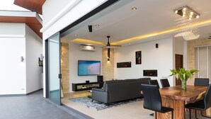 A modern living room with a dark sofa, a wooden dining table, and black chairs. - Villa Victoria (Koh Samui)
