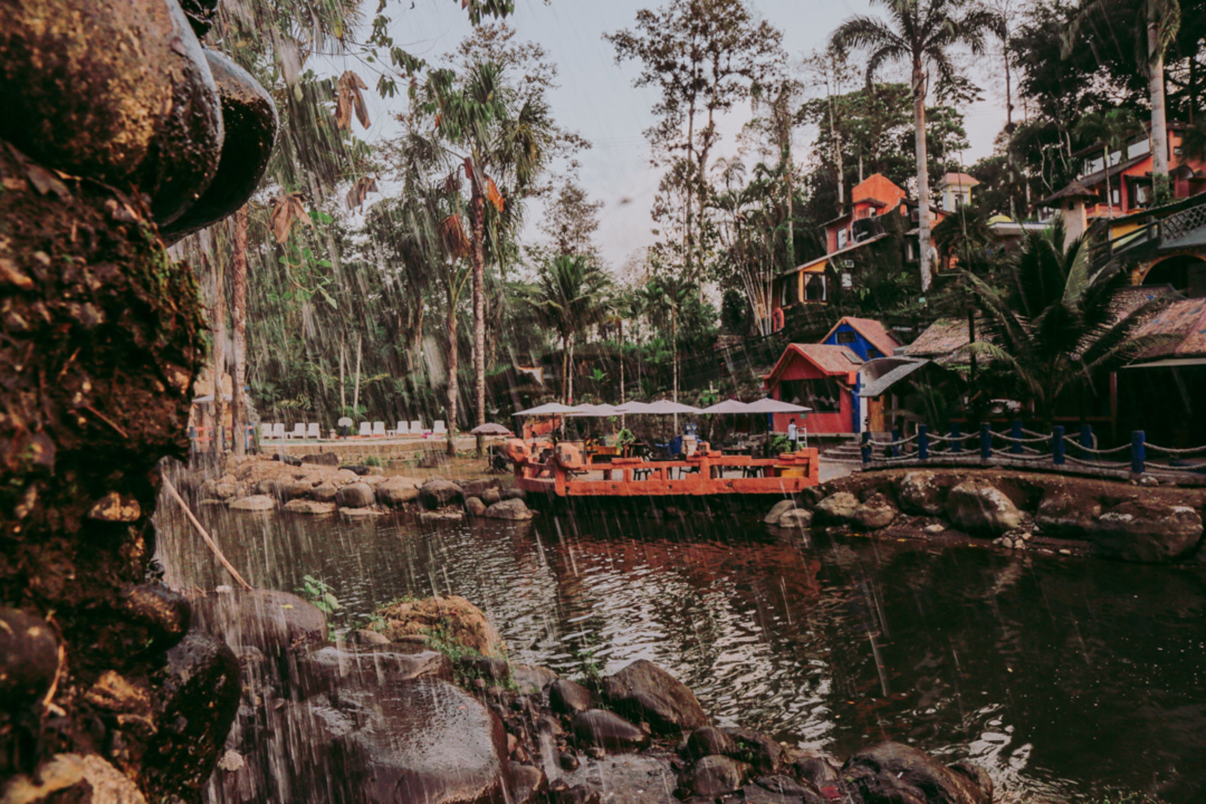 A riverside view with a boat dock, rocky terrain, and buildings in the background.