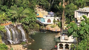 A waterfall cascading into a river, surrounded by lush greenery and traditional buildings with arched windows and a bridge. - Kashama Eco Resort y Spa (Valle Hermoso)