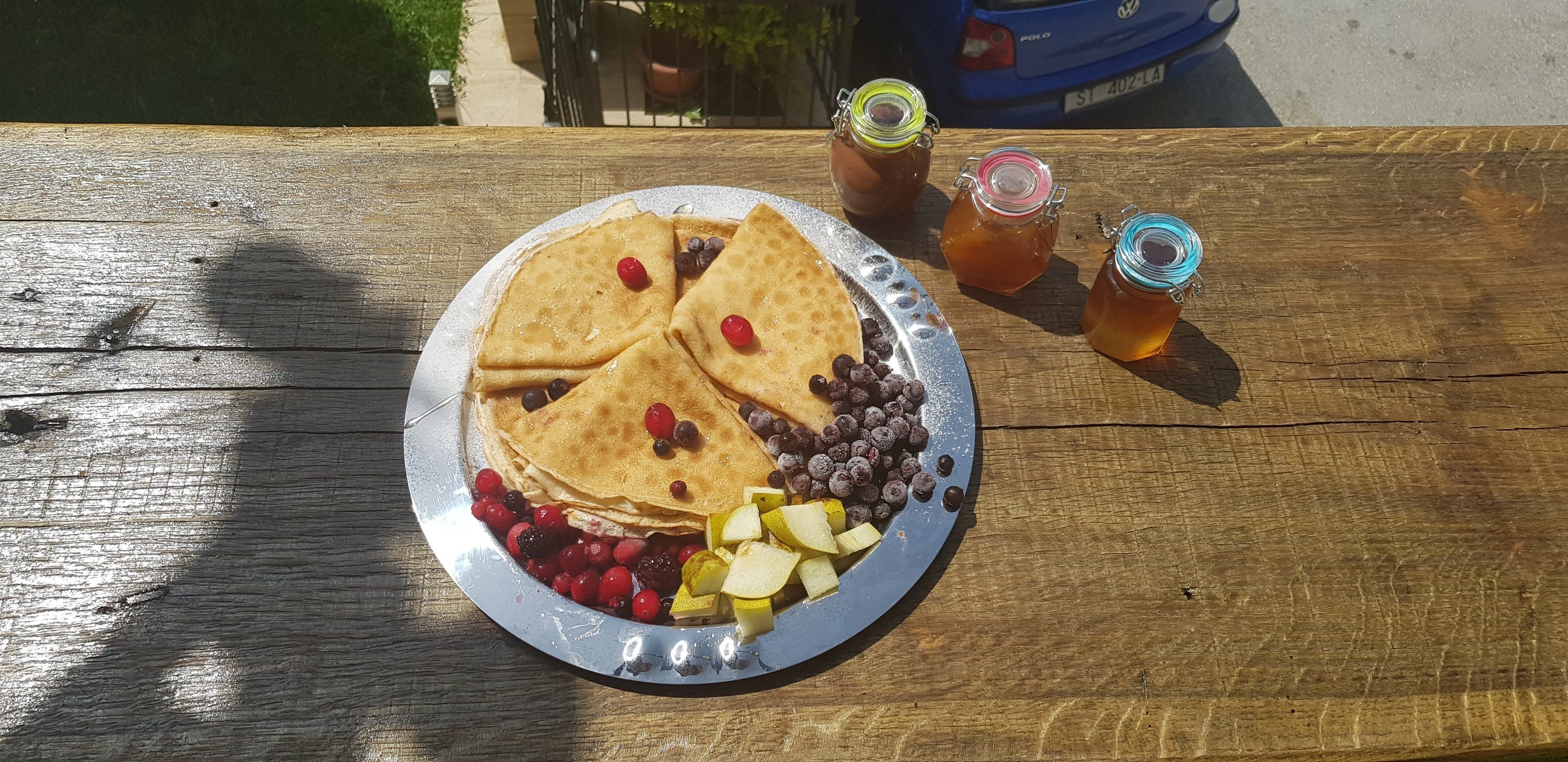 A plate of crepes with berries and a jar of honey on a wooden table.