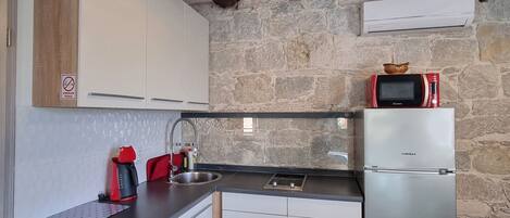Una cucina compatta con parete in pietra, travi in legno, frigorifero in acciaio inox, forno a microonde e macchina da caffè.
