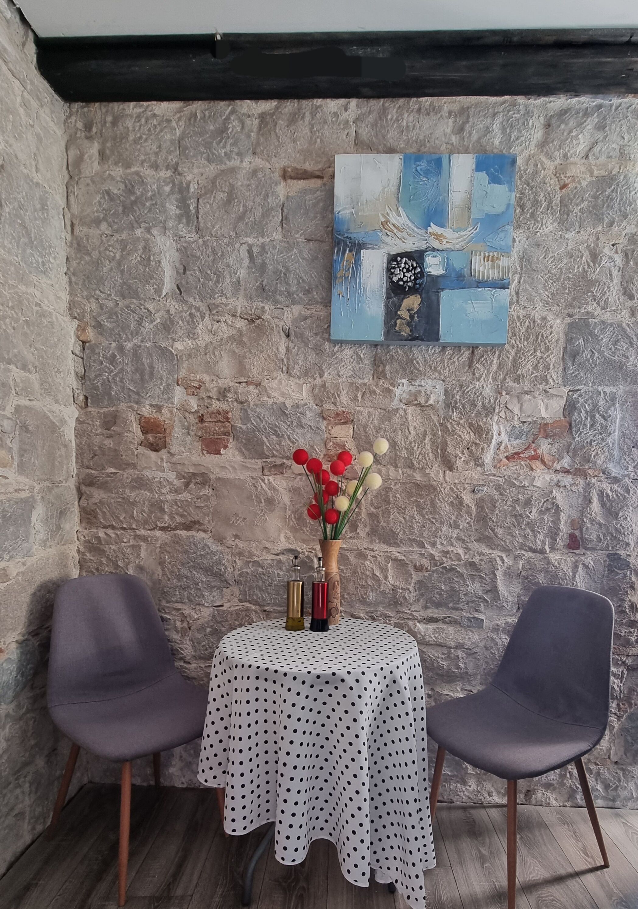 Una stanza d'angolo con parete in pietra, un tavolo a pois, due sedie e un vaso con fiori.