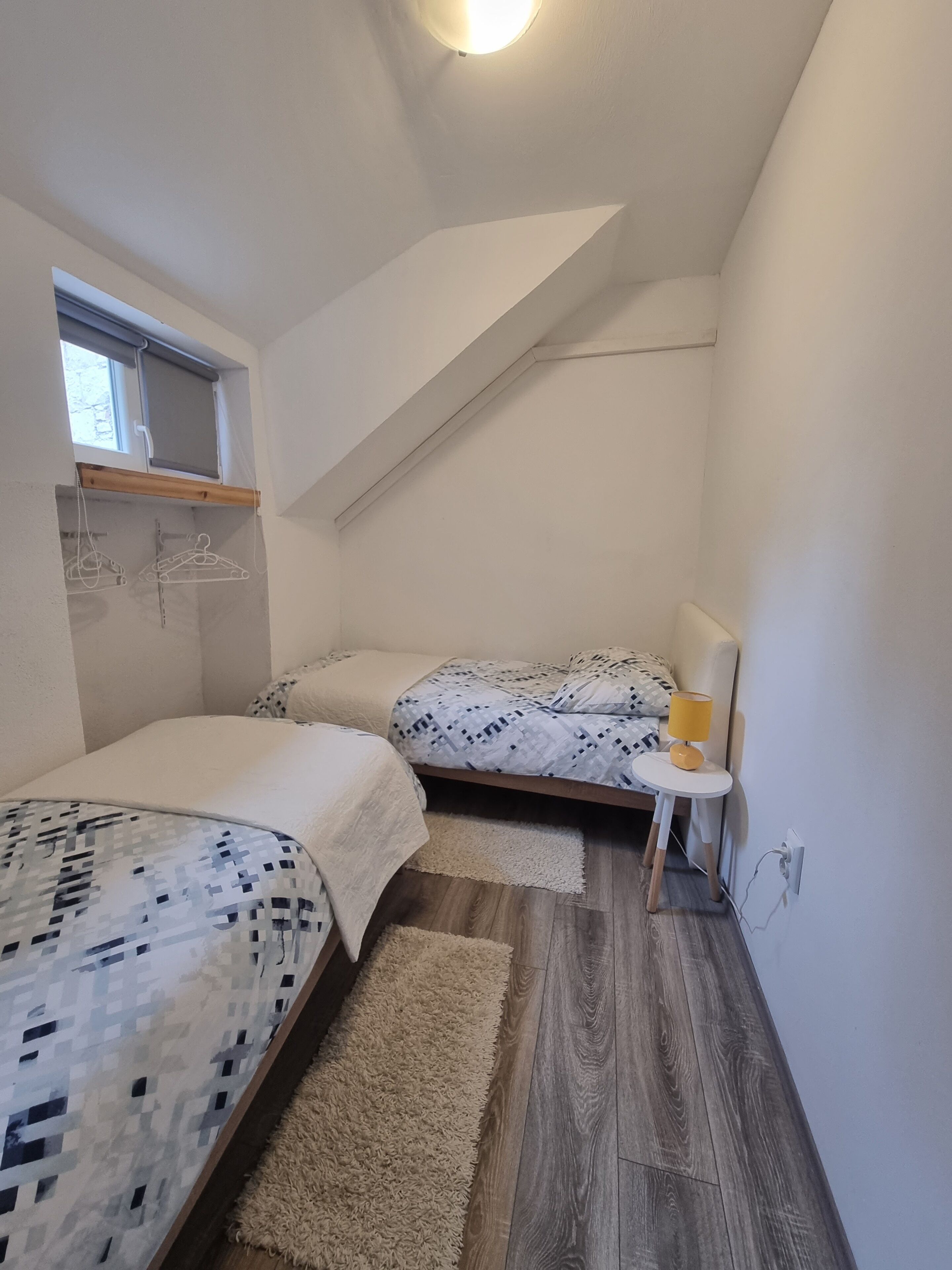 A small, well-lit bedroom with two beds, a small table, and a window.