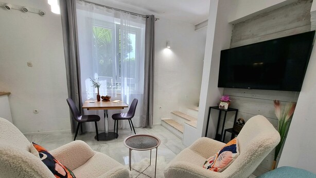 A modern living room with two plush armchairs, a dining table with chairs, a small round table, a flat-screen TV mounted on the wall, and a staircase leading to an upper level. - Apartment Trumbic (Split)