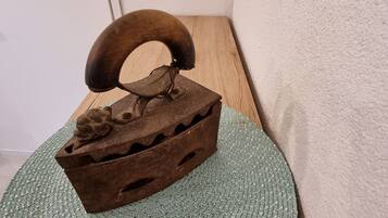 A rustic wooden chest with a curved handle on a woven mat, placed on a wooden surface against a plain wall.