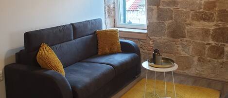 Un salon avec un canapé foncé, un tapis jaune, une petite table ronde et un mur en pierre.