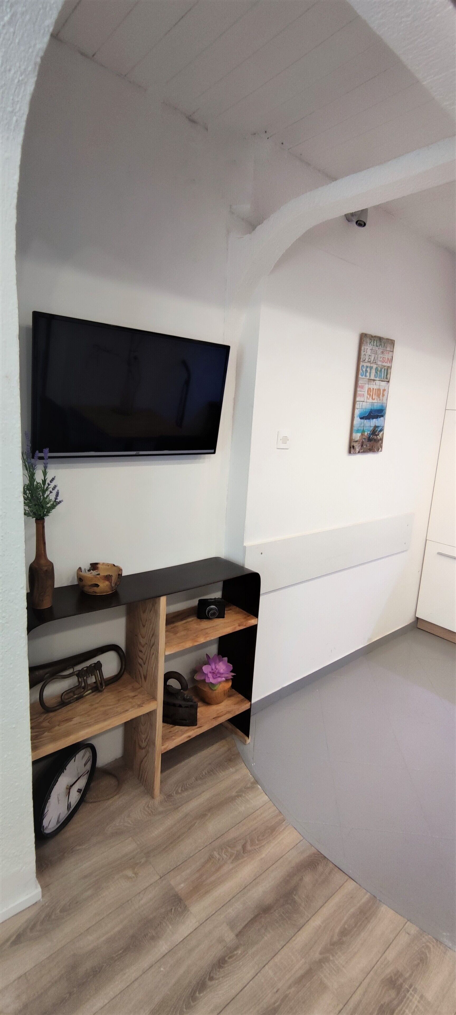 A room with a flat-screen TV mounted on the wall, wooden shelves with various items, a clock, and a poster on the wall.