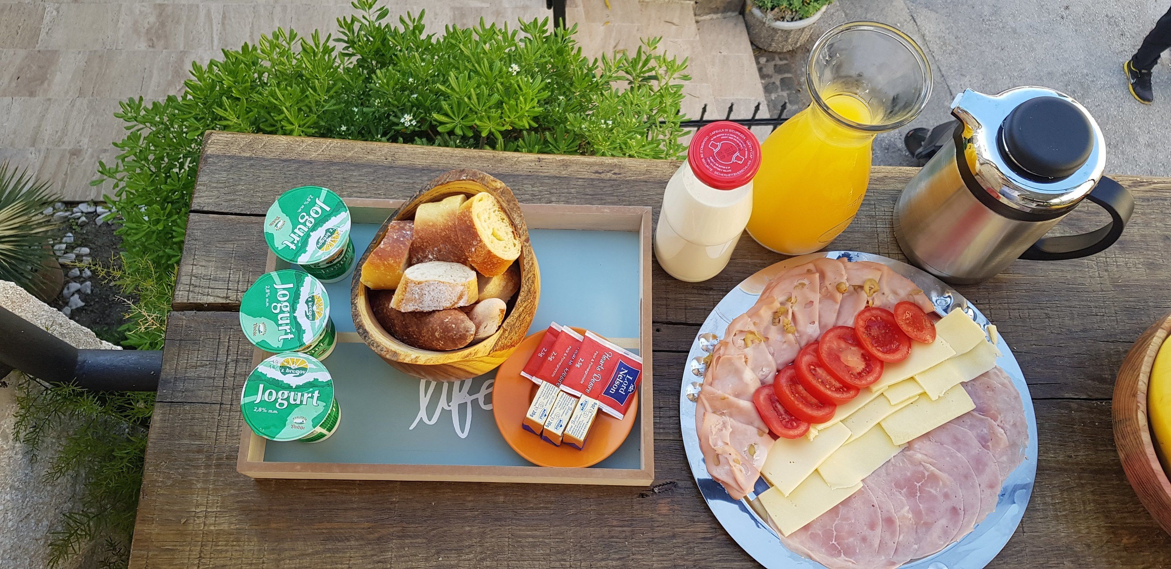 Una mesa de madera con una bandeja que contiene pan, mantequilla, mermelada y una botella de jugo.