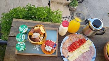 Una mesa de madera con un desayuno que incluye pan, yogur, queso, jamón, tomates y una banana.