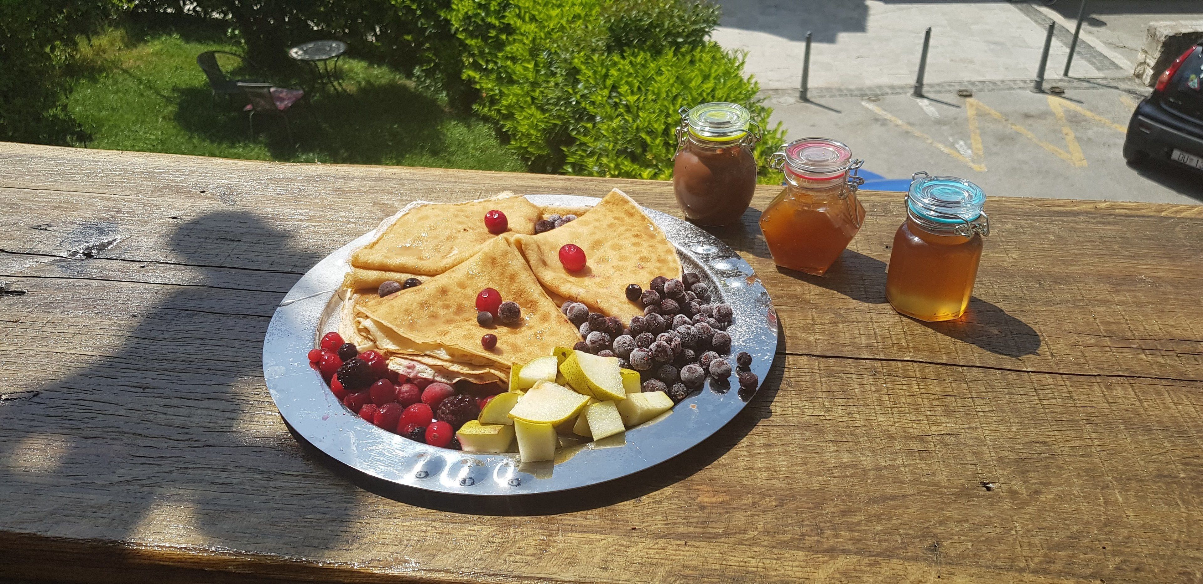 Un plato de tortitas con bayas y manzanas, y dos frascos de miel sobre una mesa de madera.