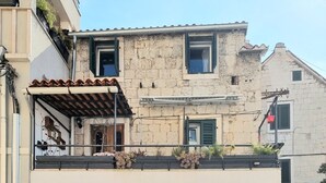 A two-story building with a balcony, a door with a window, and a small garden area with potted plants. - Apartment Trumbic (Split)