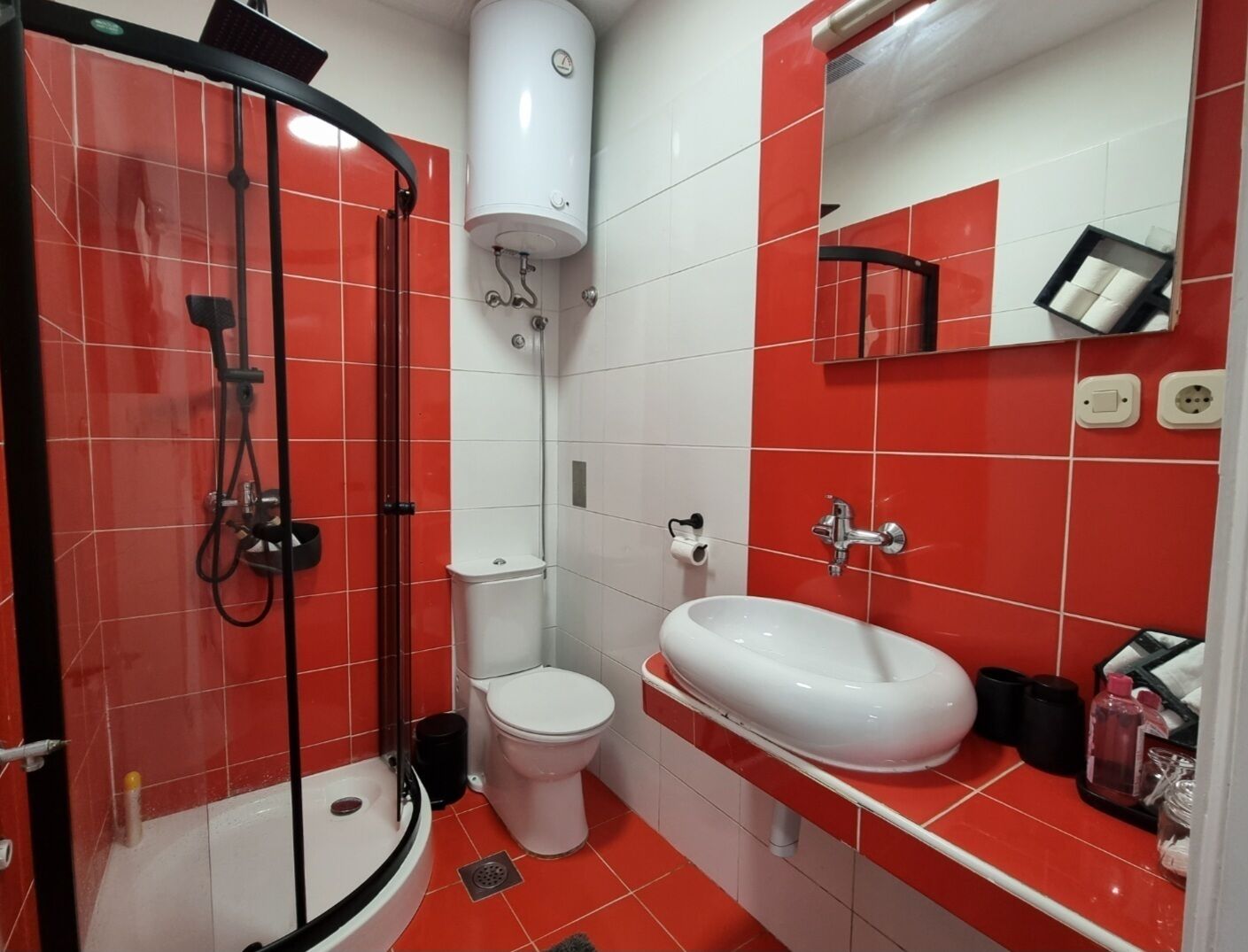 A bathroom with a shower, toilet, and sink, featuring red and white tiles.