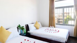 A hotel room with two beds, a window with curtains, an air conditioner, and a small table with a plant and a calendar. - Hue Royal Hotel (Hue)