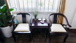 A room with two wooden chairs, a small table with a vase and a plate, and a large potted plant. - Hue Royal Hotel (Hue)