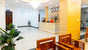A hotel reception area with a wooden reception desk, a chandelier, and several wooden chairs. - Hue Royal Hotel (Hue)