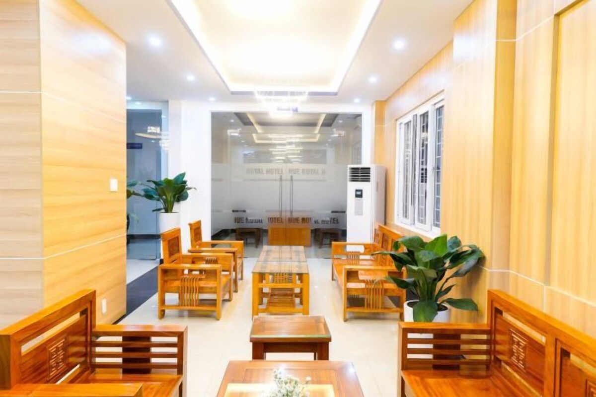 A hotel lobby with wooden furniture, a reception desk, and a large potted plant.
