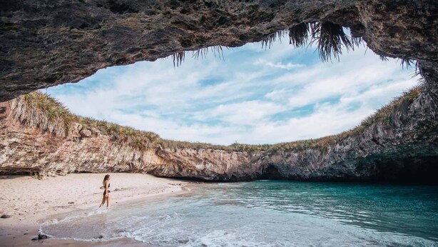 A beach with a cave entrance, clear water, and a person standing on the sand. - Amaia Boutique Hotel (Sayulita)