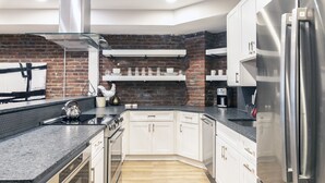 Une cuisine moderne avec des armoires blanches, un réfrigérateur en acier inoxydable et un mur de briques en guise de crédence.