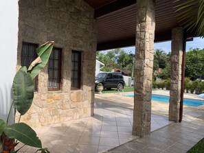 Um edifício de pedra com alpendre coberto, piscina e um SUV estacionado.
