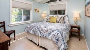 A bedroom with a large bed, two bedside tables, and a window with blinds.