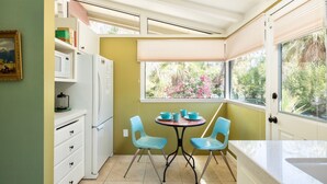 A compact kitchen with a dining table, chairs, a refrigerator, and a window with a view of greenery.