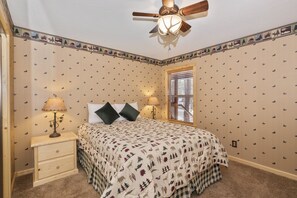 Un dormitorio con cama, dos mesitas de noche, ventilador de techo y ventana con persianas.