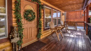 A wooden cabin with a porch, a welcome sign, and Christmas decorations. - Mountain Bliss by Destination Big Bear : Remarkable Single Story Log Style Home in Pinewood Estates! Outdoor Hot Tub! Arcade! (Big Bear City)