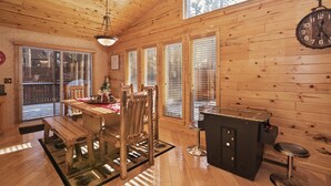 A wooden interior with a dining table, chairs, a bar area, and a clock on the wall. - Mountain Bliss by Destination Big Bear : Remarkable Single Story Log Style Home in Pinewood Estates! Outdoor Hot Tub! Arcade! (Big Bear City)