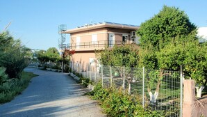 A residential building with a paved driveway, surrounded by greenery and a metal fence. - Sirens House (Platanias)