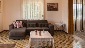 A living room with a sofa, a table with decorative items, a painting on the wall, and an air conditioning unit. - Sirens House (Platanias)