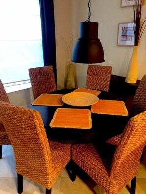 A dining area with a round table surrounded by wicker chairs, a black pendant light, and a vase with branches. - Estero Private Pool Home (Estero)