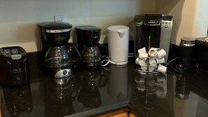 Een keuken met houten kastjes, een zwart aanrecht en verschillende koffiezetapparaten, waaronder een Keurig.