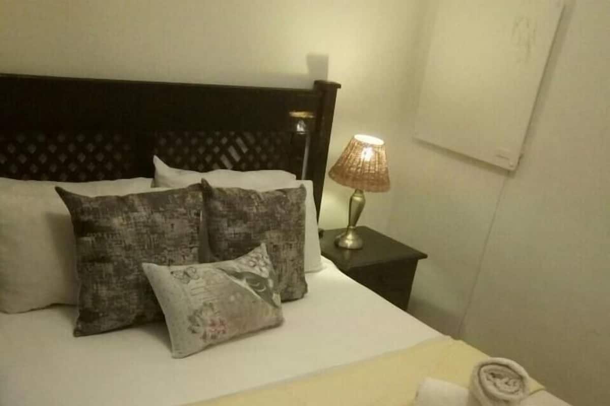 Cama bem arrumada com colcha bege, dois travesseiros e uma toalha enrolada ao lado.