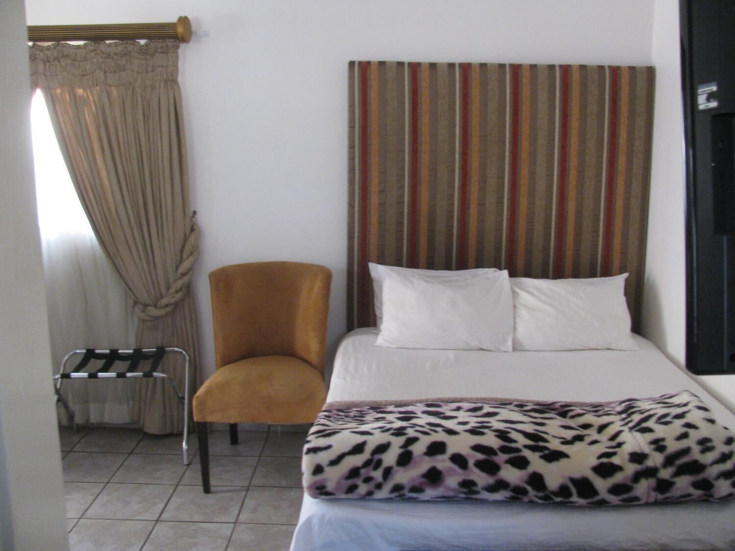 Une chambre d’hôtel avec un lit, une chaise, une tête de lit à rayures et une fenêtre avec des rideaux.